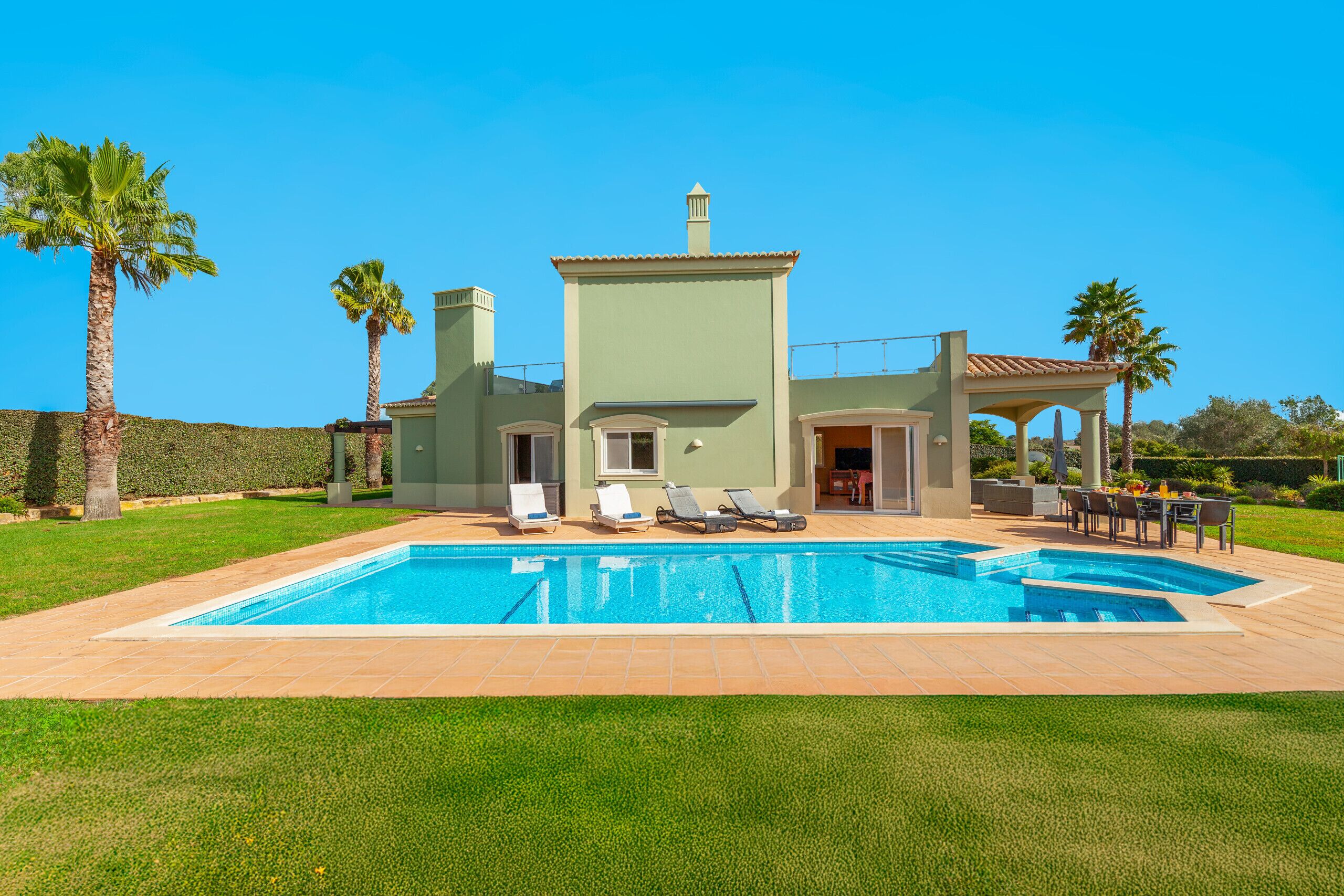 A modern house with a swimming pool, outdoor seating, and palm trees.