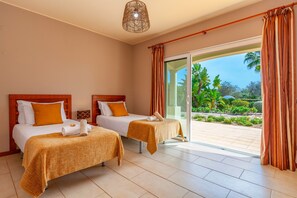 Une chambre d’hôtel avec deux lits, une grande porte-fenêtre coulissante donnant sur un jardin et un luminaire suspendu.