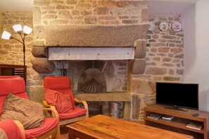 Ein Steinkamin mit einem Fernseher auf einem Holzboden, ein rotes Sessel und ein Holztisch.