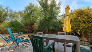 An outdoor patio with a table and chairs, surrounded by greenery and trees. - Gîte Les Pâturages, Larmor-Plage: Private Terrace, Garden, and Wi-Fi (Larmor-Plage)