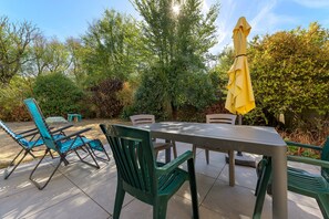 Eine Terrasse im Freien mit Tisch und Stühlen, umgeben von Pflanzen und Bäumen.