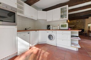 Cuina compacta amb armaris blancs, rentadora integrada i cafetera.
