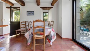 A dining area with a table set for four, wooden chairs, a view through a glass door, and a framed picture on the wall. - Gîte Les Pâturages, Larmor-Plage: Private Terrace, Garden, and Wi-Fi (Larmor-Plage)