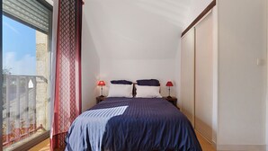 A bedroom with a bed, two bedside lamps, a window with curtains, and a view of the outside. - Gîte Les Pâturages, Larmor-Plage: Private Terrace, Garden, and Wi-Fi (Larmor-Plage)