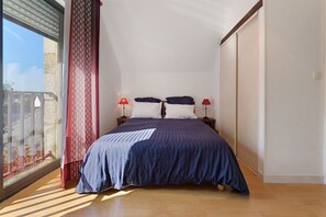 Ein Schlafzimmer mit einem Bett, zwei Nachttischlampen, einem Fenster mit Vorhängen und Blick ins Freie.