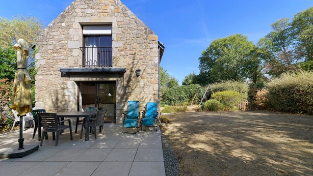 A stone building with a balcony, outdoor seating, and a gravel path. - Gîte Les Pâturages, Larmor-Plage: Private Terrace, Garden, and Wi-Fi (Larmor-Plage)