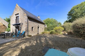 Ein Steinhaus mit geneigtem Dach, einer Terrasse mit Stühlen und einem Rasenplatz.
