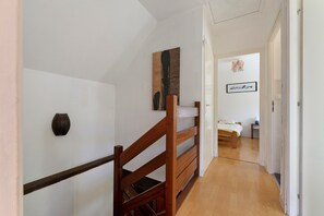 Ein Flur mit einer Holztreppe, einem Bett und einer Tür zu einem Schlafzimmer.