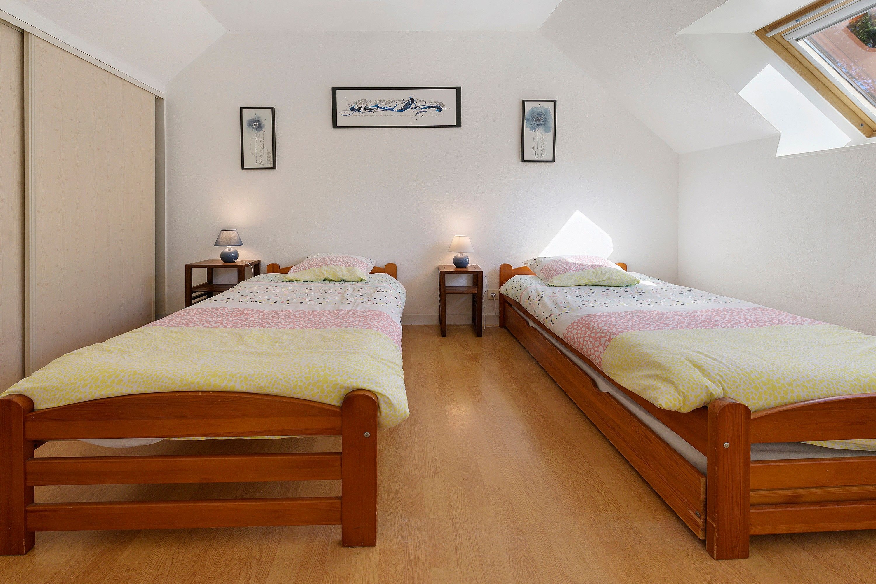 Un dormitorio con dos camas individuales, cabeceros de madera, mesitas de noche con lámparas y un tragaluz.