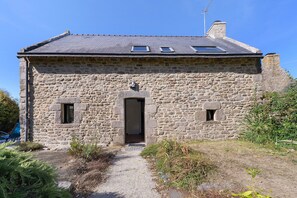 Ein Steinhaus mit geneigtem Dach, einem zentralen Eingang und zwei kleinen Fenstern im Obergeschoss.