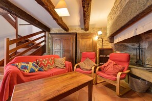Habitació acollidora amb una escala de fusta, un sofà vermell amb coixinets estampats, una taula de centre de fusta i una llar de pedra amb una làmpada penjant.