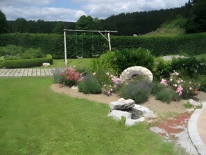 A garden with a swing set, a stone arch, and various plants.