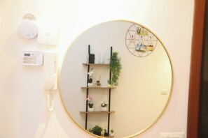 Ein Zimmer mit einem runden Spiegel, einem Pflanzenregal, einer Wanduhr und einem Thermostat.