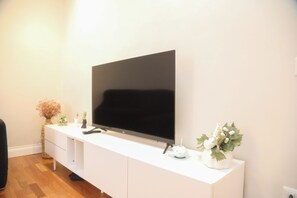 Un téléviseur à écran plat fixé sur un meuble de télévision blanc, avec une télécommande, une plante décorative et un petit objet blanc posé sur le dessus.