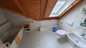 Ett litet, kompakt badrum med ett sluttande tak, ett takfönster, en toalett, ett handfat och en hylla för förvaring.