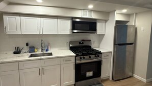 A modern kitchen with white cabinets, a stainless steel stove, a microwave, and a refrigerator. - Cozy 1-bedroom apartment in tranquil Bronx with AC and free parking (Bronx)