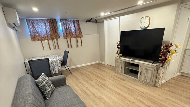 A living room with a grey sofa, a TV on a wooden stand, and a dining table with chairs. - Cozy 1-bedroom apartment in tranquil Bronx with AC and free parking (Bronx)