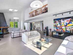 Ein großzügiger Wohnbereich mit einem modernen weißen Sofa, einem Glastisch und einem großen abstrakten Gemälde.
