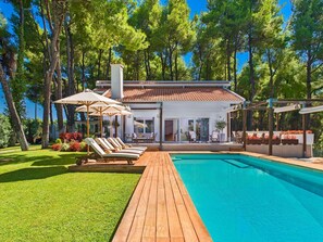 Ein modernes Haus mit Swimmingpool, Liegestühlen und Garten.