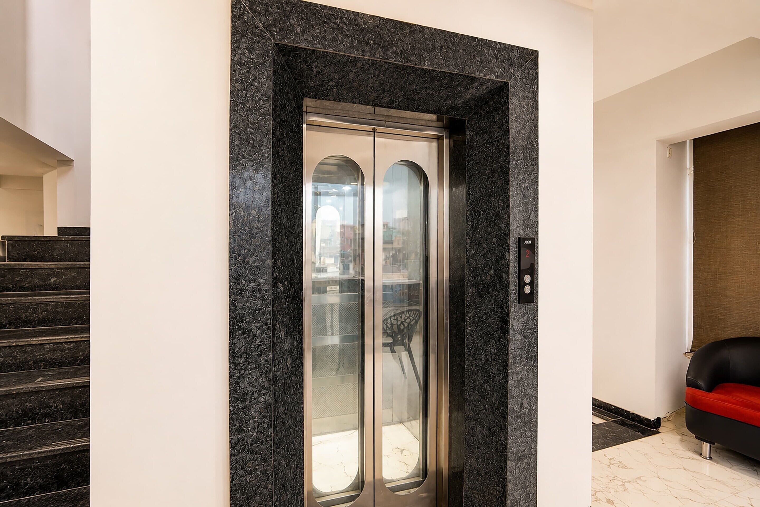 A modern elevator with a glass door, situated between a staircase and a seating area.