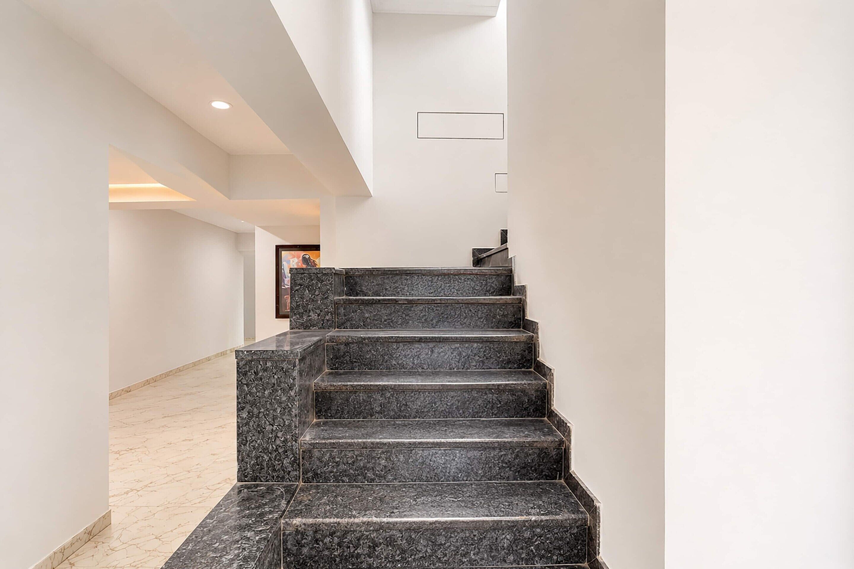 Un intérieur moderne avec un escalier menant à l’étage supérieur, des murs blancs et un sol en marbre.