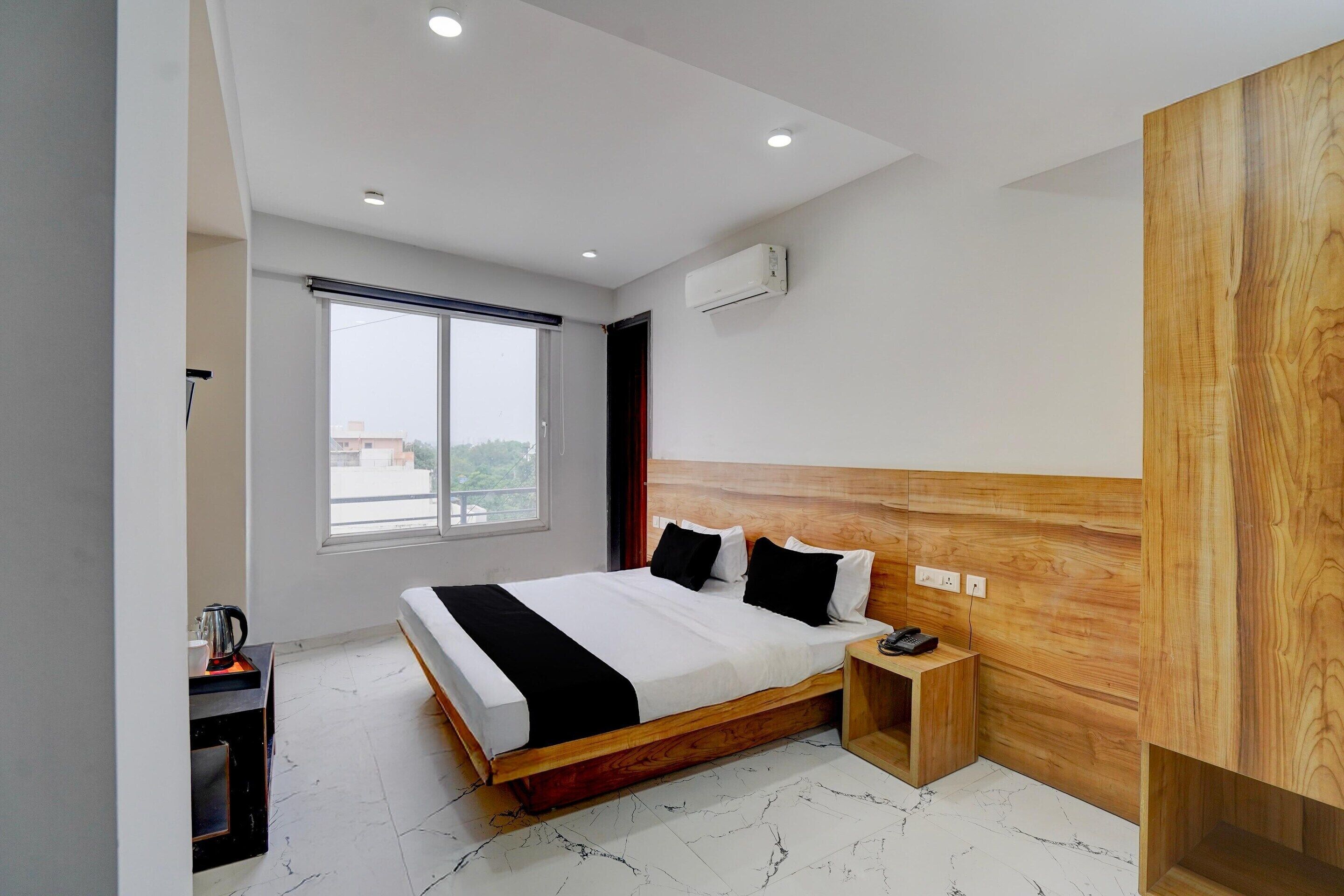 A modern hotel room with a large bed, a wooden headboard, a small bedside table, and a window with a view.