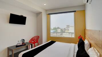 A hotel room with a bed, a desk, a chair, a television, and a window with a view of buildings.
