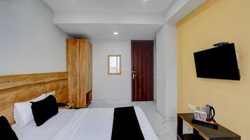 A hotel room with a bed, a wardrobe, a television, and a small table with a kettle.