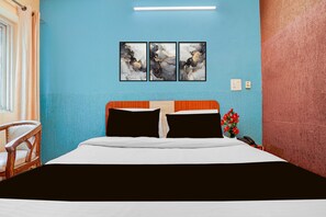 Une chambre d’hôtel avec un lit, une chaise, une table de chevet, un vase avec des fleurs et trois tableaux abstraits accrochés au mur.