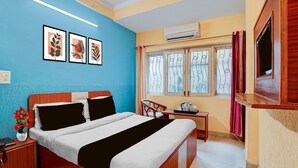 A hotel room with a bed, bedside table, a small table with a kettle, a window with curtains, and an air conditioning unit. - Deluxe Room North Star Residency (Dehradun)