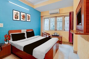 A hotel room with a bed, bedside table, a small table with a kettle, a window with curtains, and an air conditioning unit. - Deluxe Room North Star Residency (Dehradun)