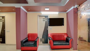 A reception area with two red and black chairs, a wall-mounted TV, and a door labeled 'WASHROOM'. - Deluxe Room North Star Residency (Dehradun)
