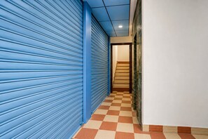 Un couloir avec une porte à volets bleus, un sol à carreaux et un escalier menant à un étage supérieur.