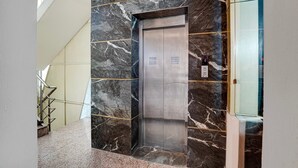 An elevator with a metallic finish, set against a marble wall with a pattern of dark and light streaks. - Deluxe Room North Star Residency (Dehradun)