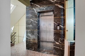 An elevator with a metallic finish, set against a marble wall with a pattern of dark and light streaks. - Deluxe Room North Star Residency (Dehradun)