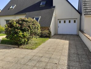 Ein Wohnhaus mit befestigter Auffahrt, einer weißen Garagentür und einem angelegten Garten.