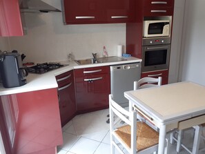 Une cuisine compacte équipée d’une cuisinière à gaz, d’un lave-vaisselle, d’un four à micro-ondes et d’une petite table à manger avec une chaise.
