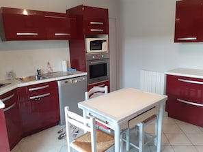 Una cuina compacta amb armaris vermells, taulell blanc, forn integrat, microones i rentaplats.