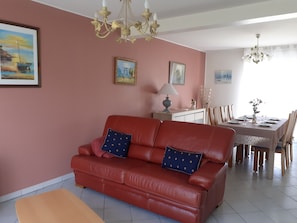 Ein Wohnzimmer mit einem roten Sofa, einem Esstisch für vier Personen und einer Chandelüster.