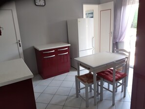 Une cuisine compacte avec un plan de travail blanc, un meuble rouge, une table blanche et deux chaises dotées de coussins rouges.