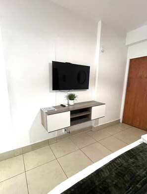 A bedroom with a bed, a TV mounted on the wall, a small plant on a console table, and a door. - Stay Car-Free in the Heart of Condado (San Juan)