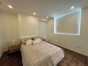 A bedroom with a bed, nightstands, a wall-mounted light, and a window with a view.