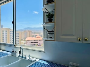 A kitchen with a window, a sink, and a shelf with a plant. - Margarita moderno Piscina, agua y parking (Porlamar)