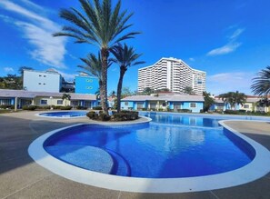 Hotel amb una gran piscina, palmeres i un edifici modern amb teulada corba.
