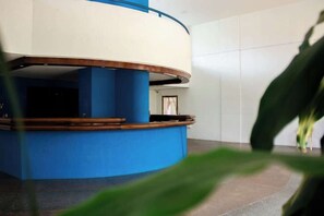 Ein runder Empfangstresen mit blauem Fuß und weißer Arbeitsfläche, umgeben von einer weißen Wand.