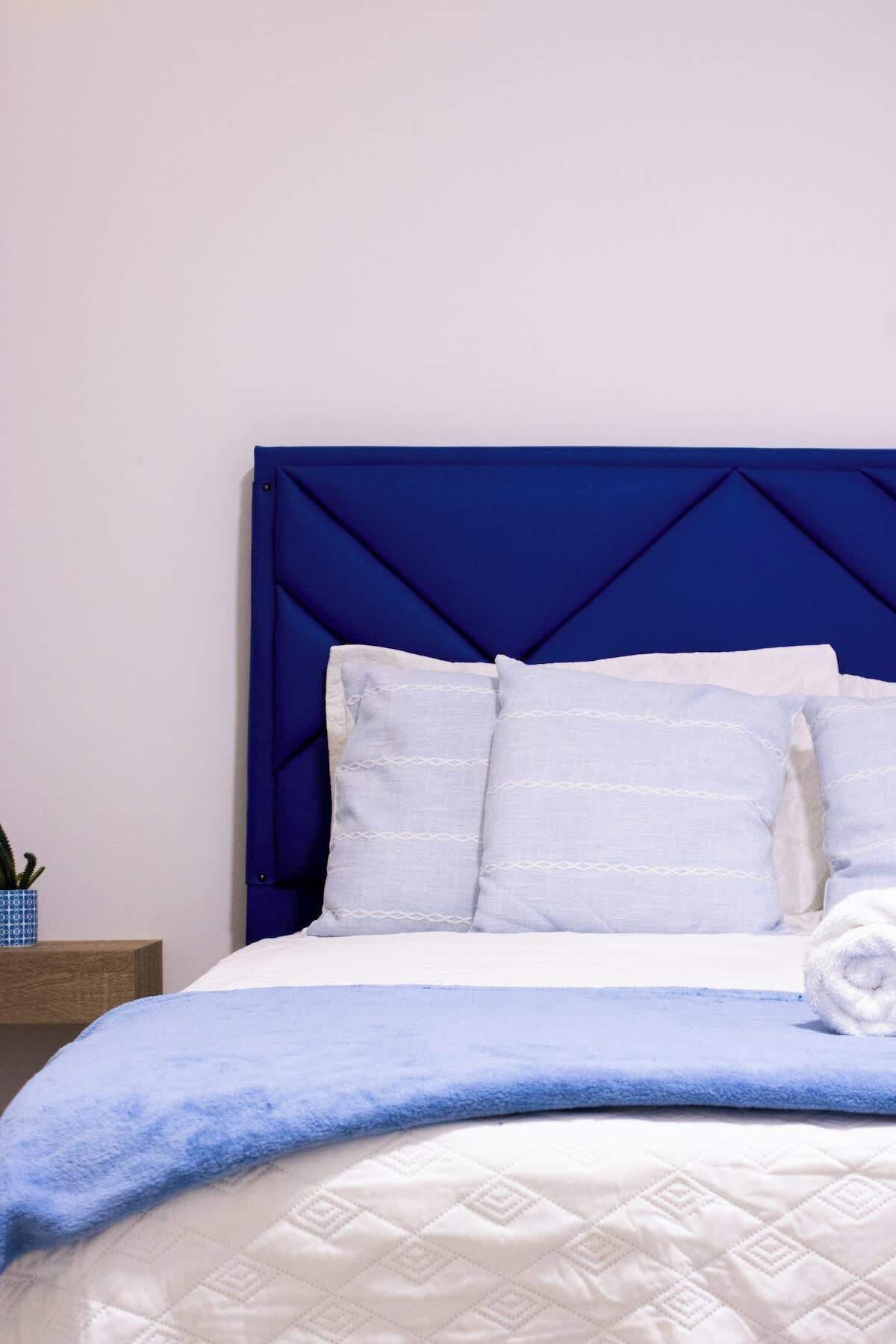 Un lit avec une tête de lit bleue, une literie blanche et une couverture bleue.