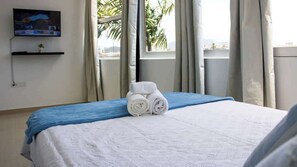 Habitación de hotel con cama, televisor montado en la pared y ventana con cortinas.