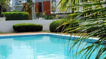 Une piscine à l’eau d’un bleu cristallin, entourée d’arbustes aux formes soignées et d’un mur blanc.