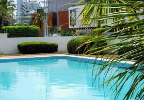 A swimming pool with clear blue water, surrounded by neatly trimmed bushes and a white wall.