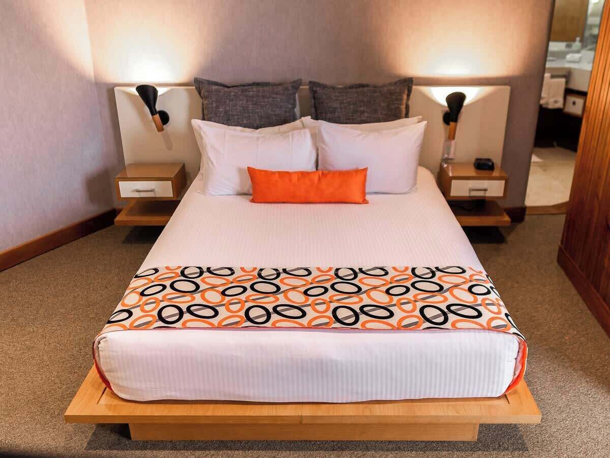 A neatly made bed with a patterned bedspread, two bedside tables with lamps, and a mirror on one of the tables.